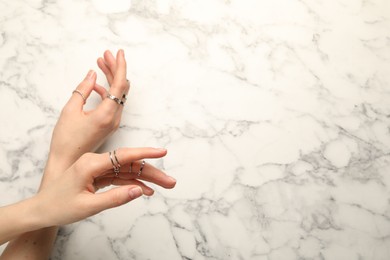 Woman wearing beautiful rings at white marble table, top view. Space for text