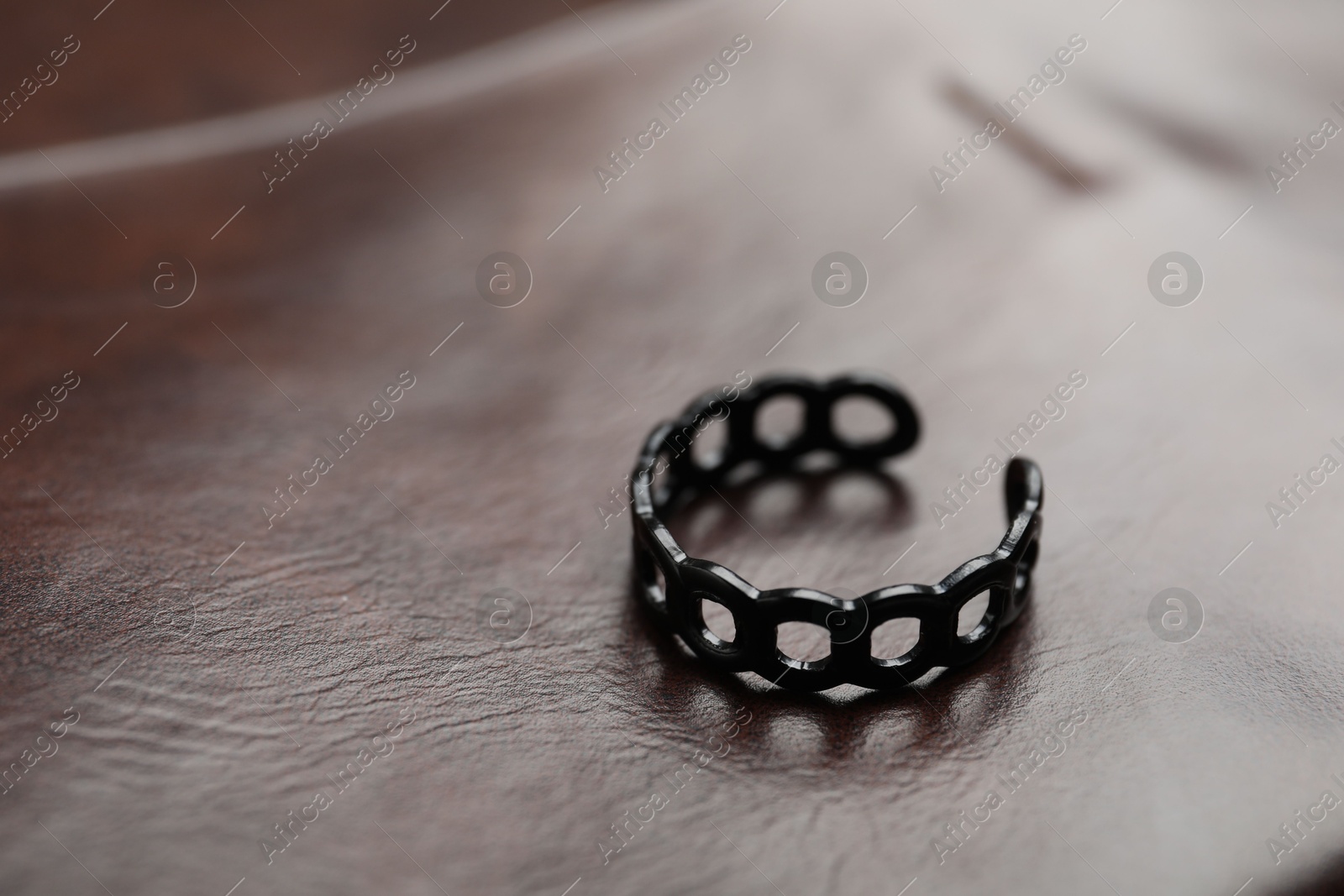 Photo of One black ring on leather surface, closeup. Space for text