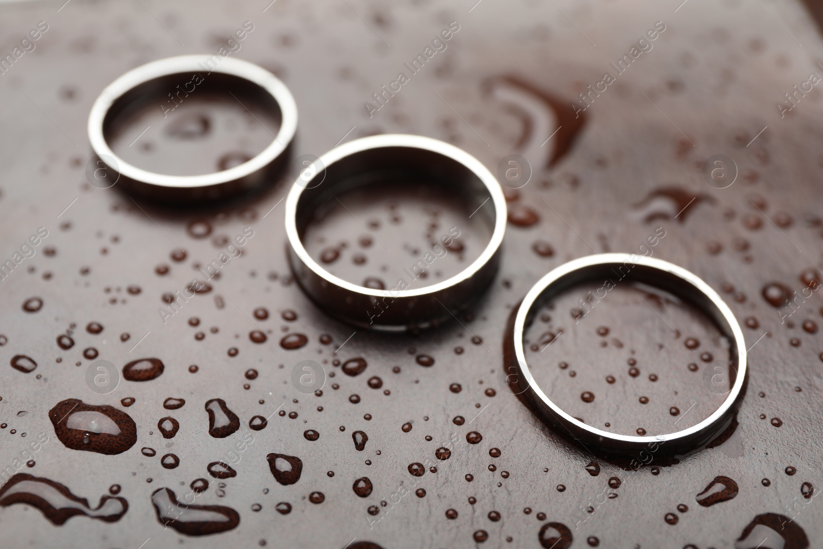 Photo of Stylish rings on leather surface with drops, closeup