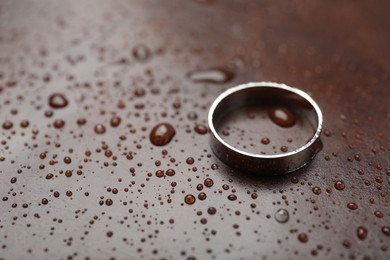 Photo of One stylish ring on leather surface with drops, closeup. Space for text