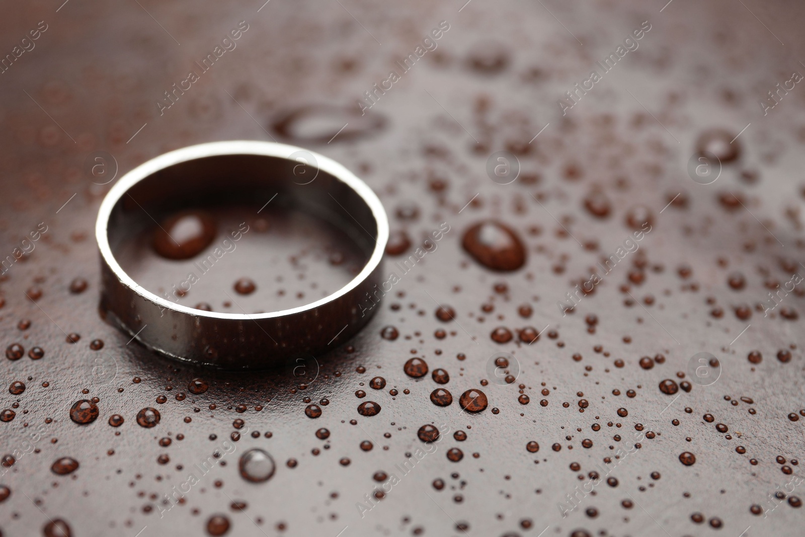 Photo of One stylish ring on leather surface with drops, closeup. Space for text