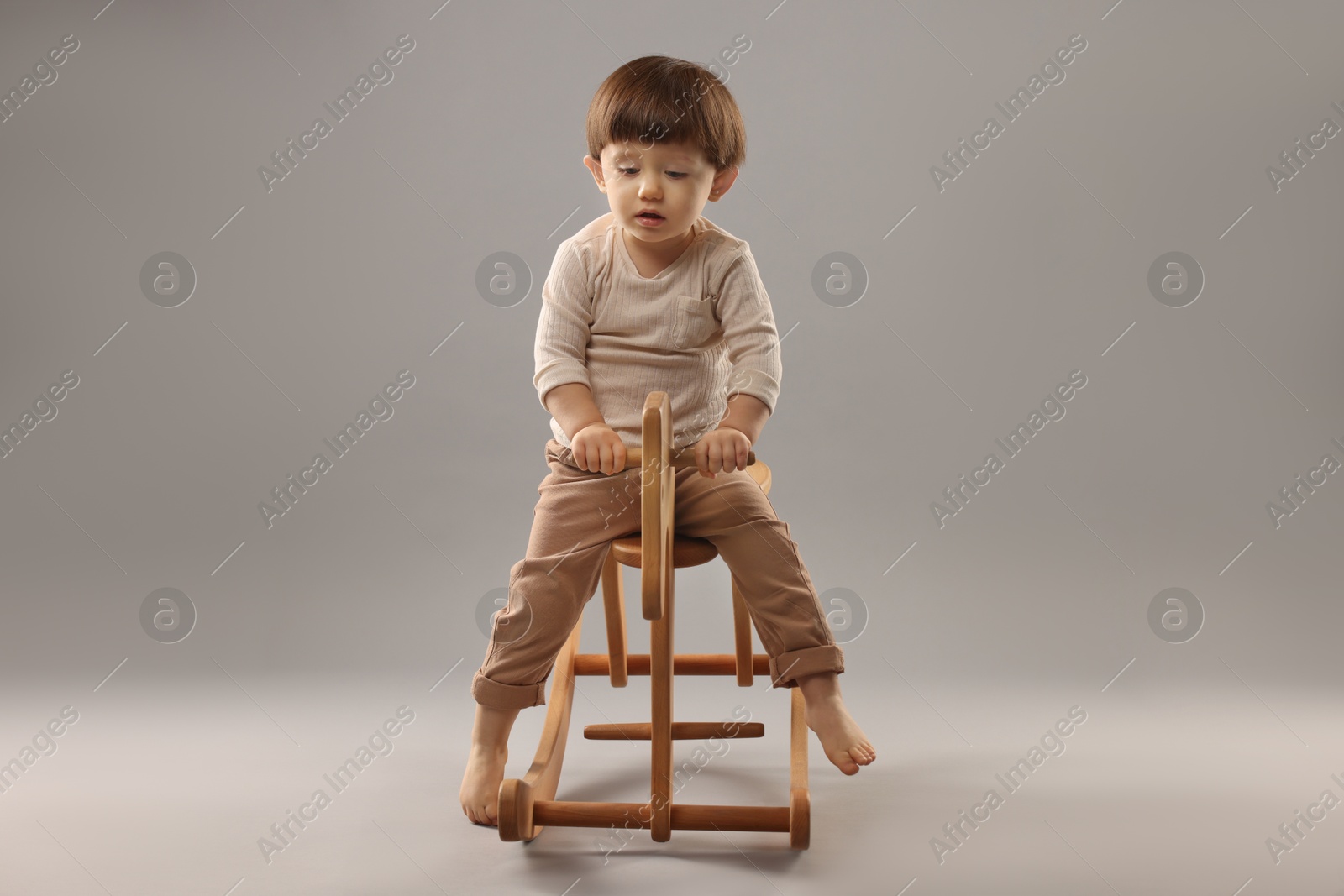 Photo of Cute little boy on wooden rocking horse against grey background