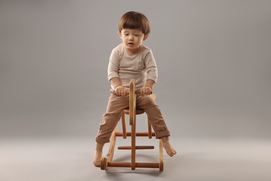 Cute little boy on wooden rocking horse against grey background