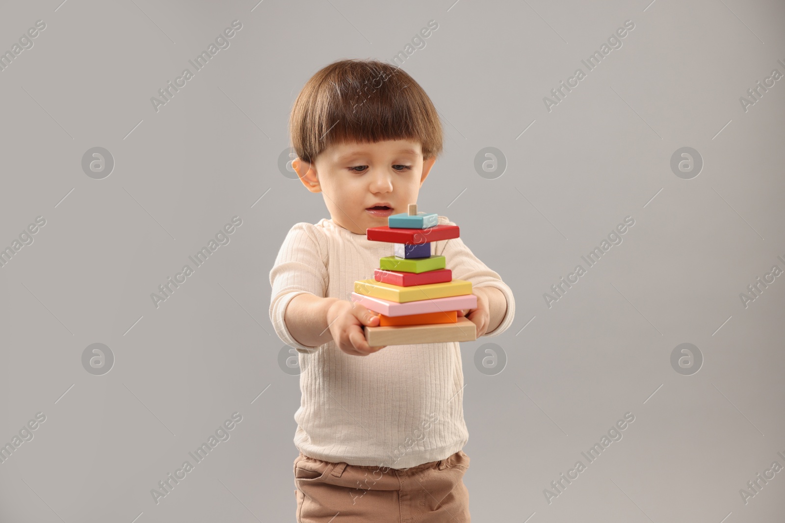 Photo of Cute little boy with colorful toy pyramid on grey background