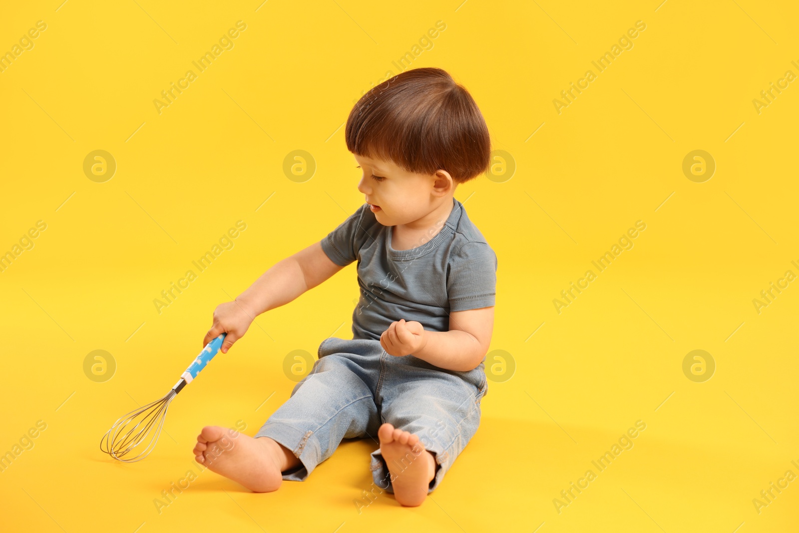 Photo of Cute little boy playing with whisk on yellow background