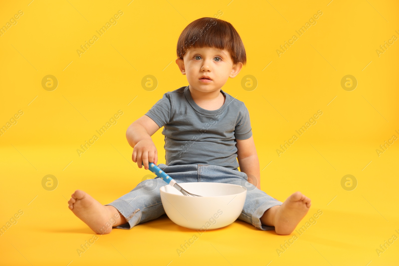 Photo of Cute little boy with bowl and whisk on yellow background