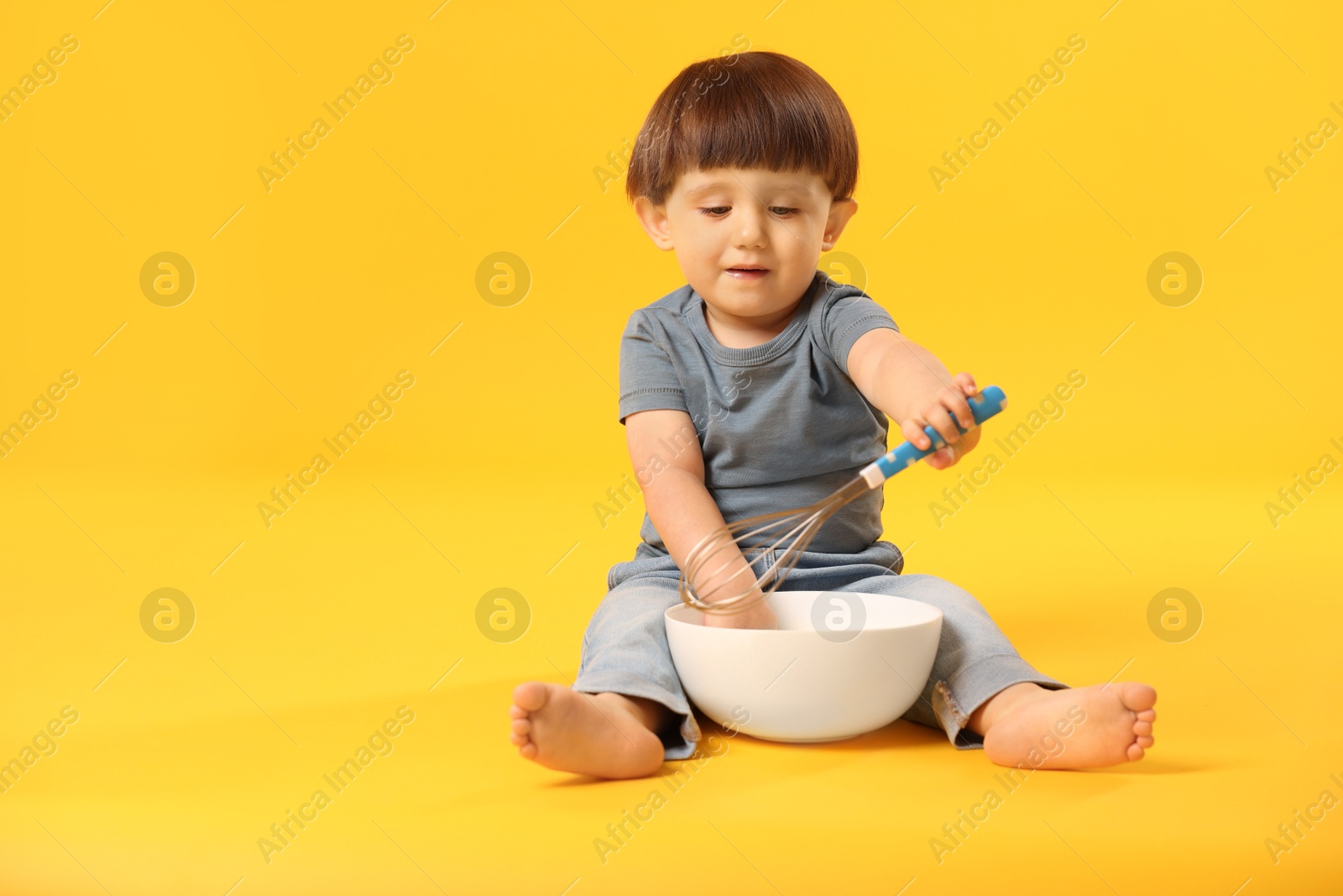 Photo of Cute little boy with bowl and whisk on yellow background. Space for text