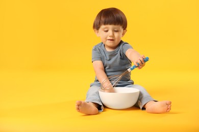 Photo of Cute little boy with bowl and whisk on yellow background. Space for text