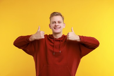 Photo of Happy man showing thumbs up on yellow background. Like gesture