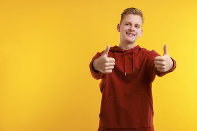 Photo of Happy man showing thumbs up on yellow background, space for text. Like gesture