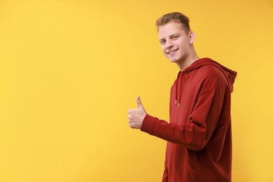 Happy man showing thumbs up on yellow background, space for text. Like gesture