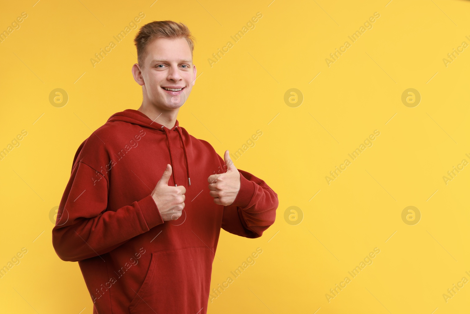 Photo of Happy man showing thumbs up on yellow background, space for text. Like gesture