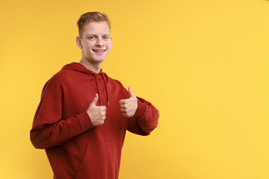 Photo of Happy man showing thumbs up on yellow background, space for text. Like gesture