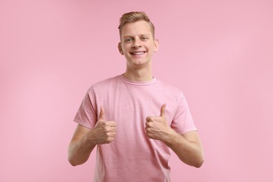 Photo of Happy man showing thumbs up on pink background. Like gesture