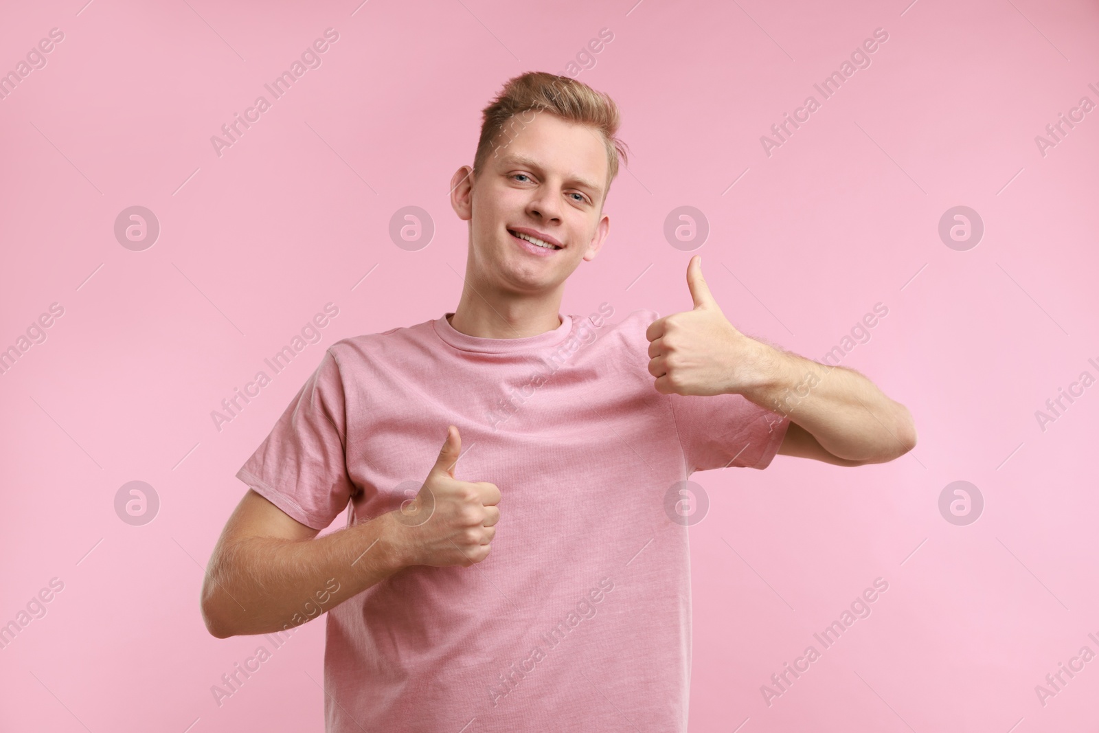 Photo of Happy man showing thumbs up on pink background. Like gesture