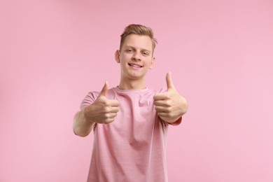 Photo of Happy man showing thumbs up on pink background. Like gesture