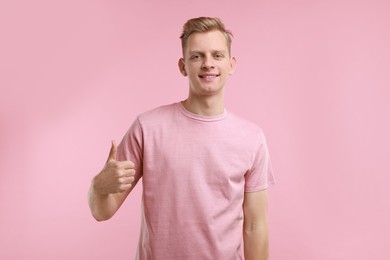 Photo of Happy man showing thumbs up on pink background. Like gesture