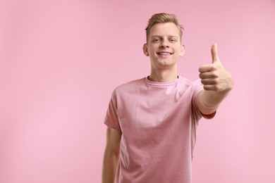 Photo of Happy man showing thumbs up on pink background, space for text. Like gesture