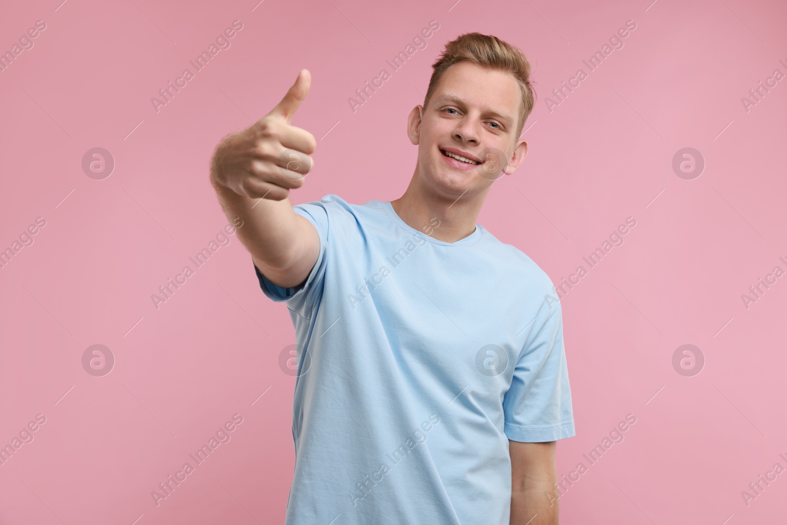 Photo of Happy man showing thumbs up on pink background. Like gesture