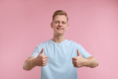 Photo of Happy man showing thumbs up on pink background. Like gesture