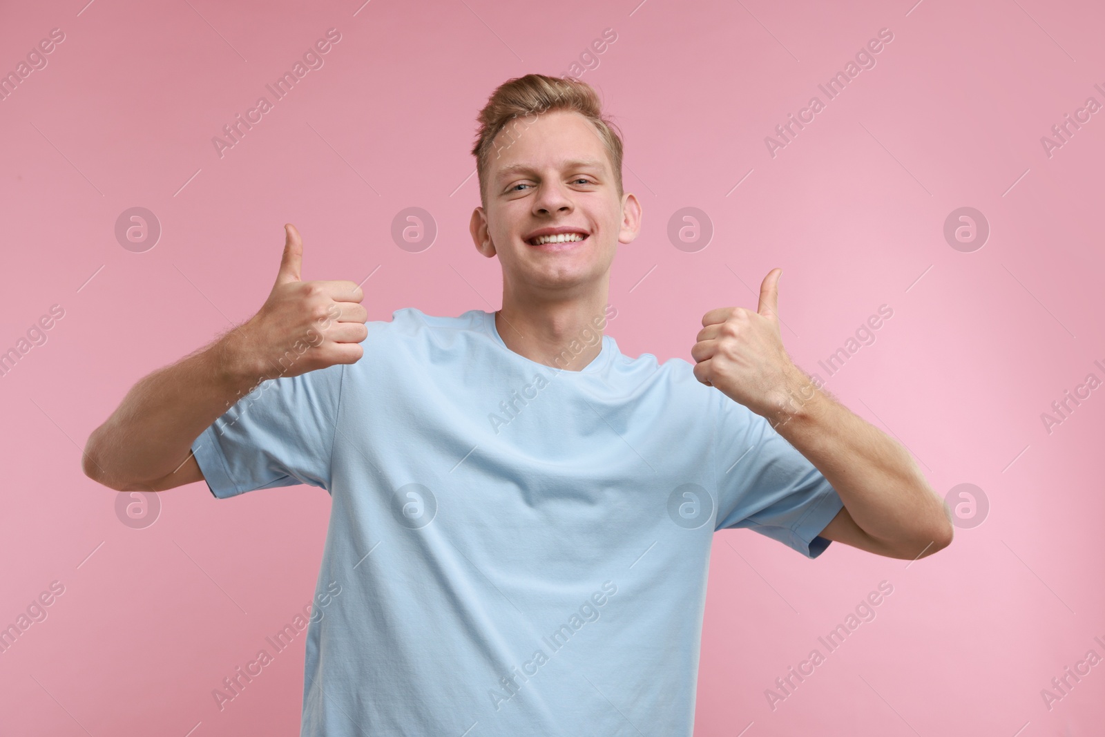 Photo of Happy man showing thumbs up on pink background. Like gesture