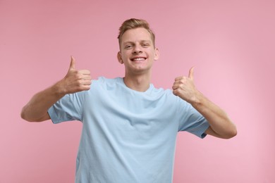 Photo of Happy man showing thumbs up on pink background. Like gesture