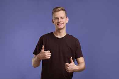 Photo of Happy man showing thumbs up on purple background. Like gesture