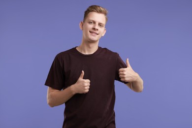 Photo of Happy man showing thumbs up on purple background. Like gesture