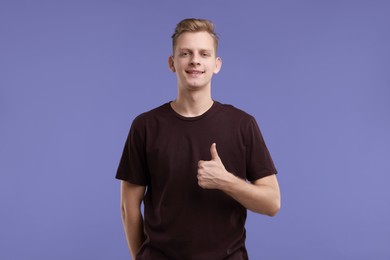 Photo of Happy man showing thumbs up on purple background. Like gesture