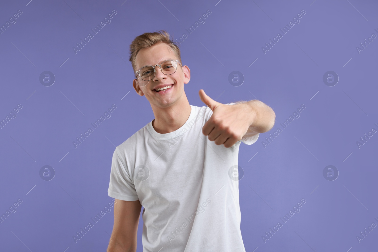 Photo of Happy man showing thumbs up on purple background. Like gesture