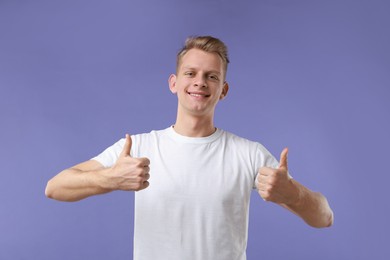 Photo of Happy man showing thumbs up on purple background. Like gesture