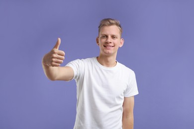 Photo of Happy man showing thumbs up on purple background. Like gesture