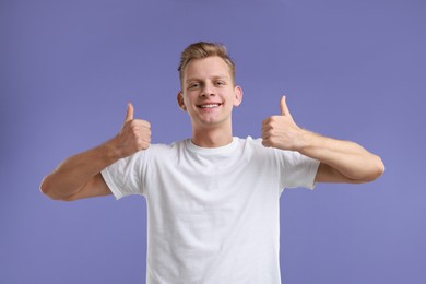 Photo of Happy man showing thumbs up on purple background. Like gesture