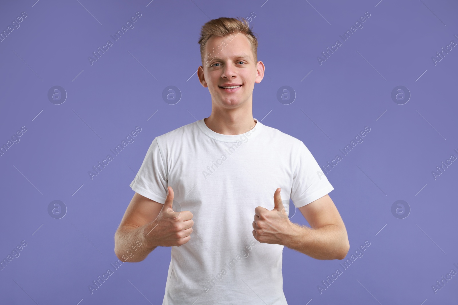 Photo of Happy man showing thumbs up on purple background. Like gesture