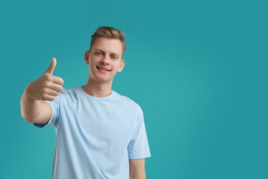 Photo of Happy man showing thumbs up on light blue background, space for text. Like gesture