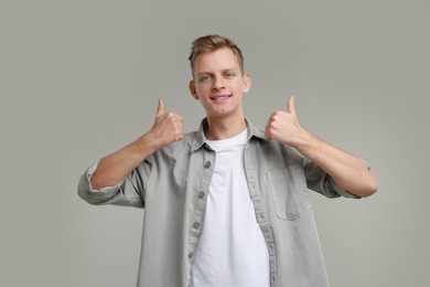 Photo of Happy man showing thumbs up on grey background. Like gesture