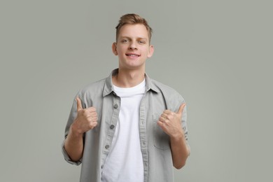 Photo of Happy man showing thumbs up on grey background. Like gesture