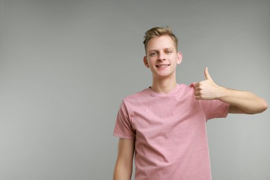 Photo of Happy man showing thumbs up on grey background, space for text. Like gesture