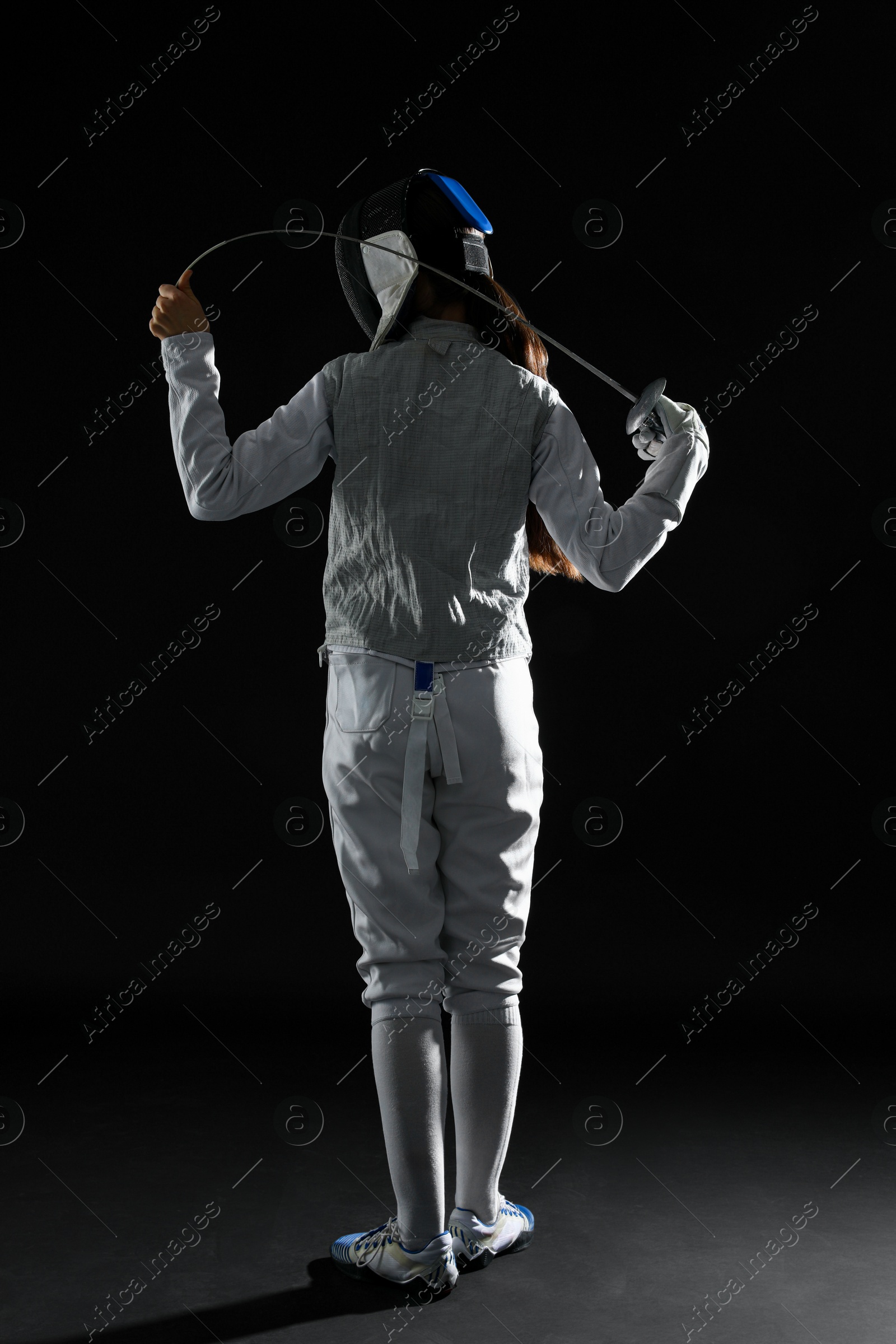 Photo of Fencer with epee on dark background, back view