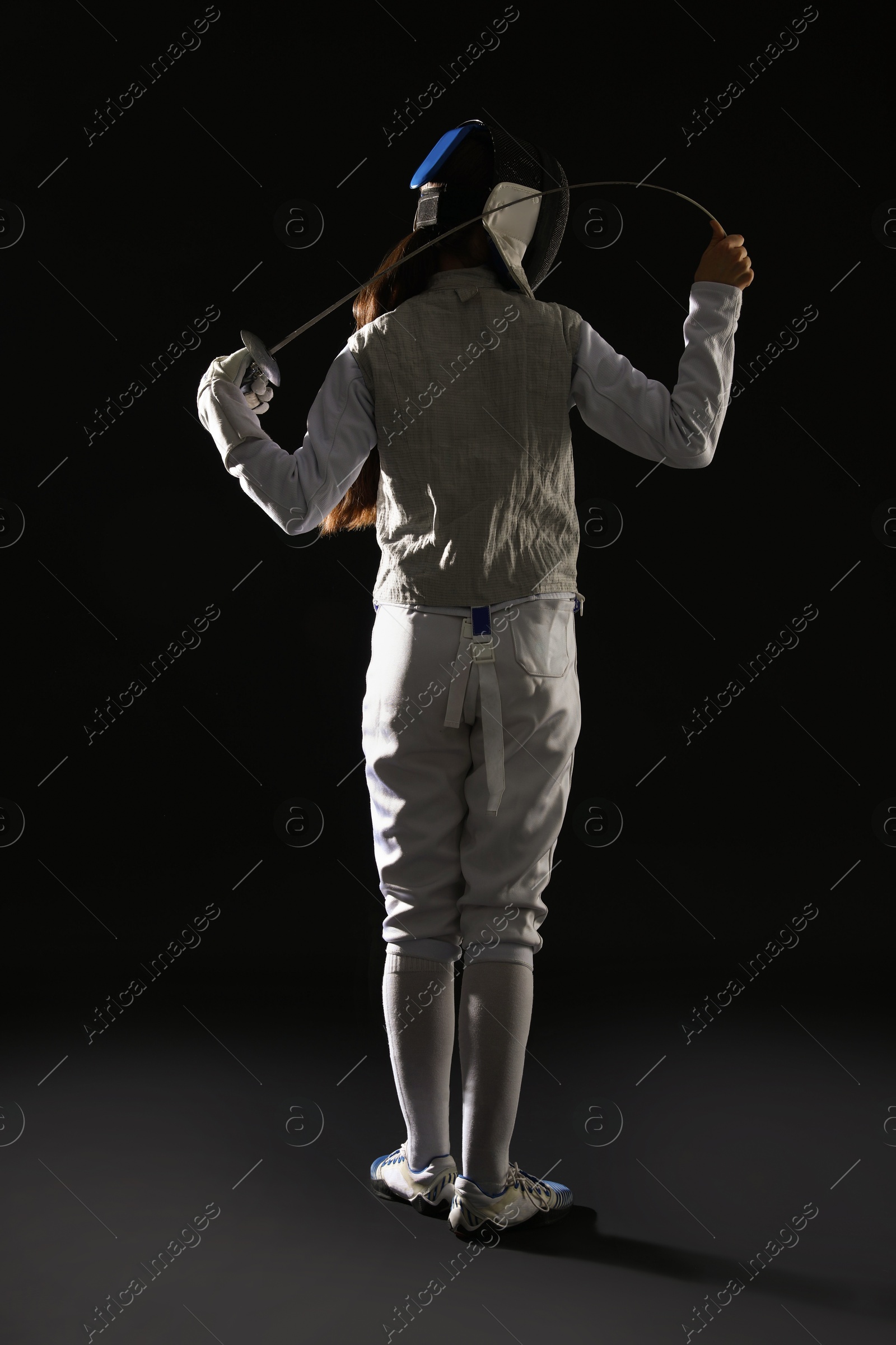 Photo of Fencer with epee on dark background, back view