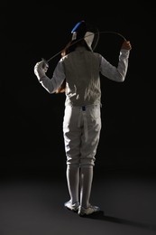 Photo of Fencer with epee on dark background, back view