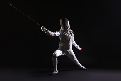 Photo of Fencer with epee practicing on dark background