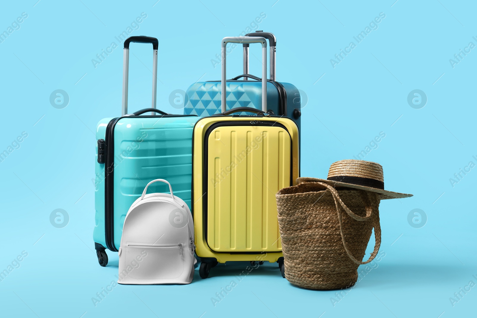 Photo of Colorful suitcases, backpack, beach bag and straw hat on light blue background