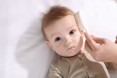 Photo of Woman brushing hair of her little baby indoors, top view. Space for text