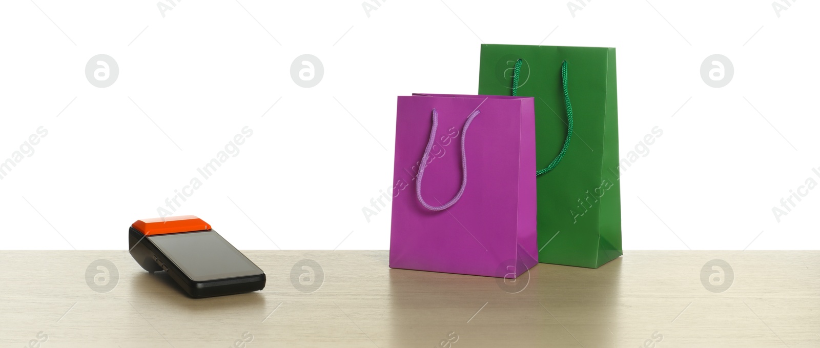 Photo of Payment terminal and shopping bags on wooden table against white background