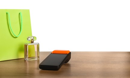 Photo of Payment terminal, perfume and shopping bag on wooden table against white background