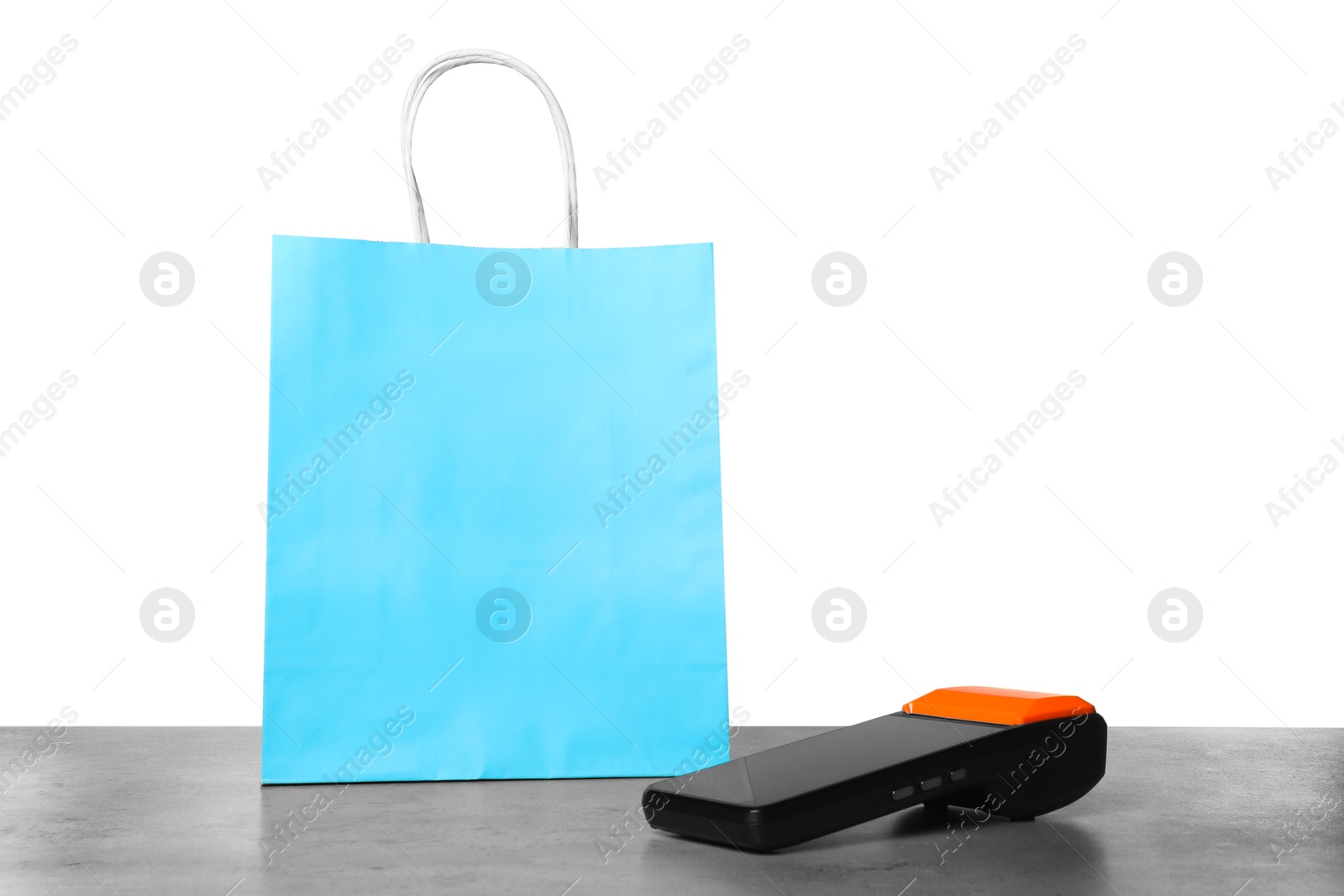 Photo of Payment terminal and shopping bag on grey table against white background