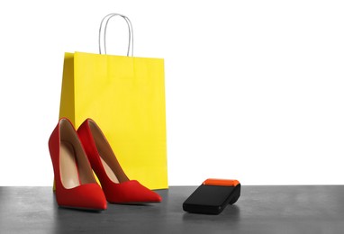 Photo of Payment terminal, shopping bag and high heeled shoes on grey table against white background