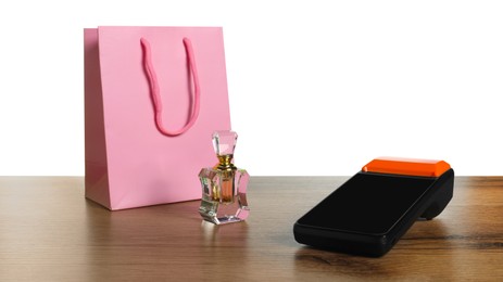 Photo of Payment terminal, perfume and shopping bag on wooden table against white background