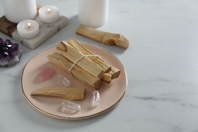 Photo of Palo santo sticks and gemstones on white table. Space for text